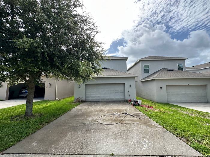 Concrete driveway pressure washing before, grey with mildew and hose laid out ready to start, two-story stucco home, Central Florida